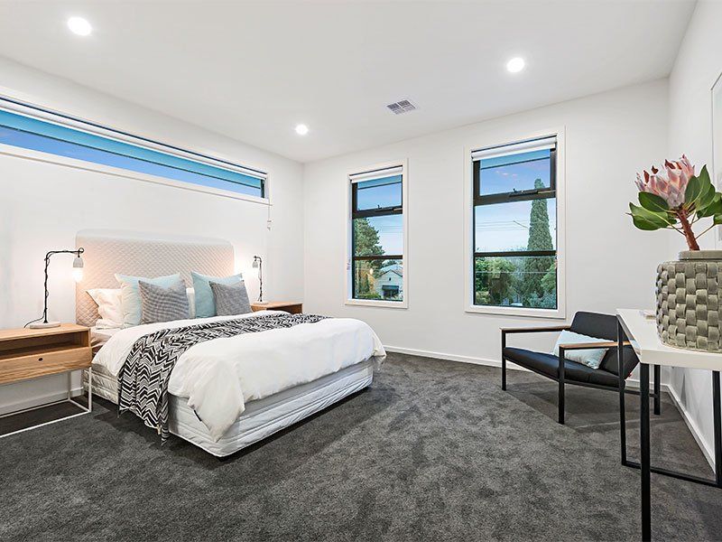 A bedroom with a bed , chair , nightstand and two windows.