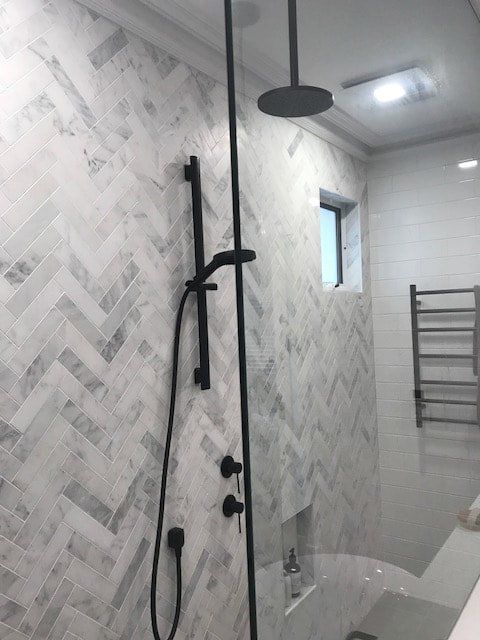 A bathroom with white tiles and a black shower head
