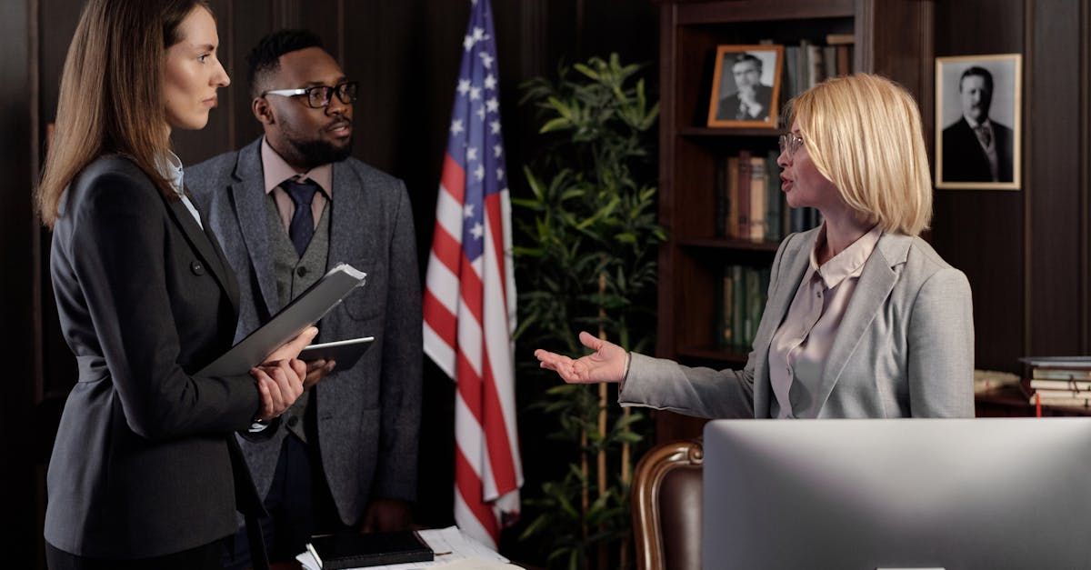 A group of people are standing in front of an american flag in an office.