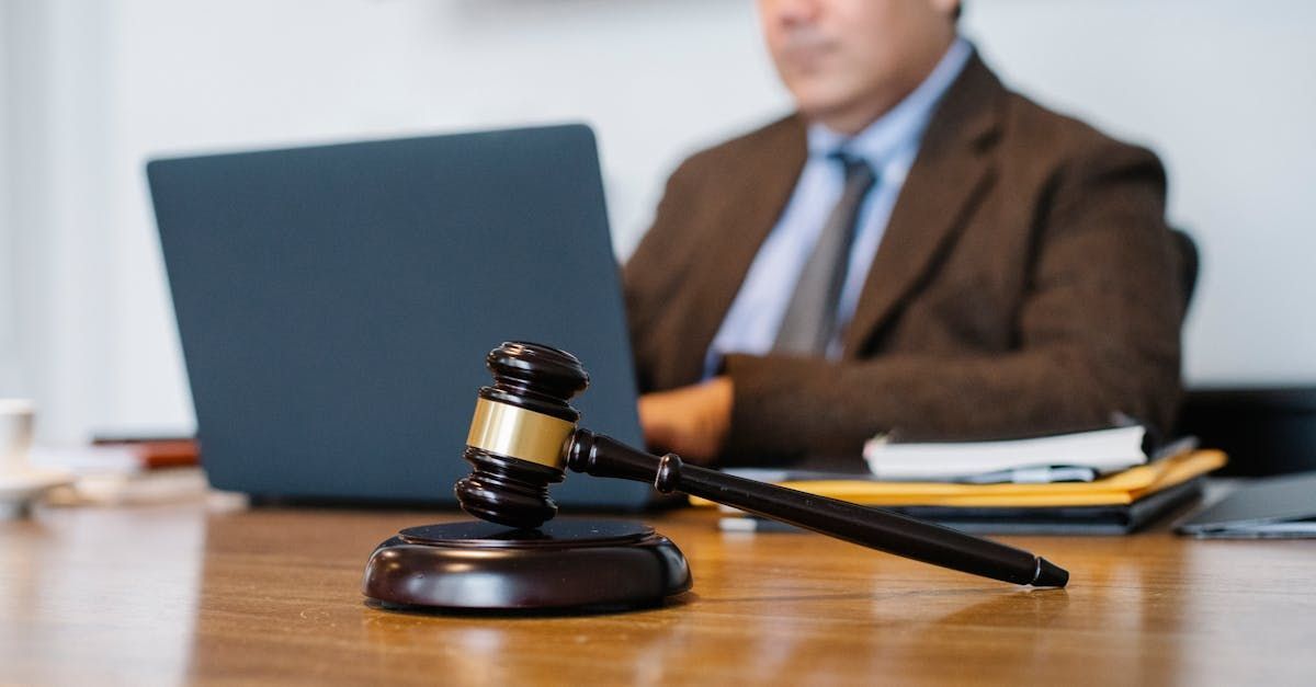 A judge is sitting at a table with a laptop and a gavel.