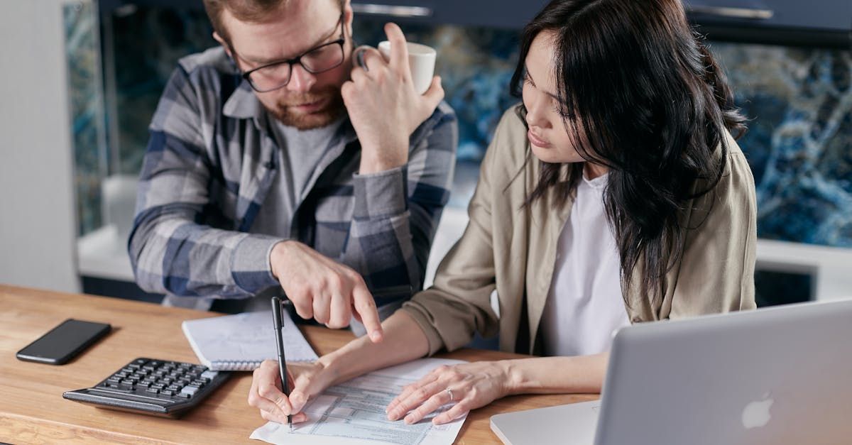 A man and a woman are sitting at a table with a laptop and a calculator.