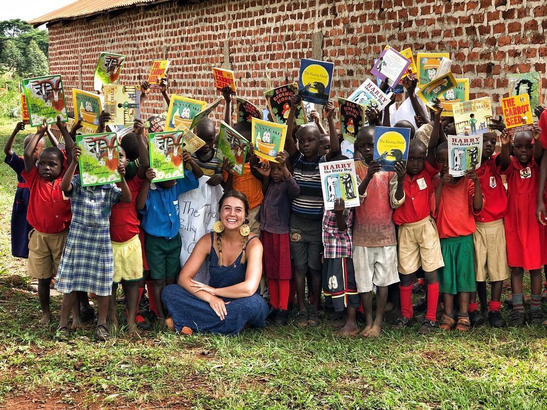 Woman seated with children holding up books in front of a brick building.