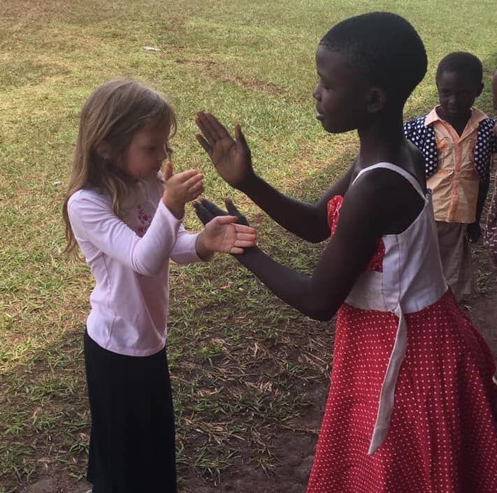 Brown haired little girl and Ugandan girl playing hand clap game