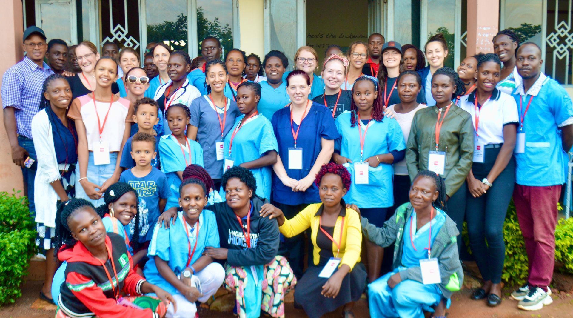 Group photo of people, many wearing blue scrubs, smiling outdoors.
