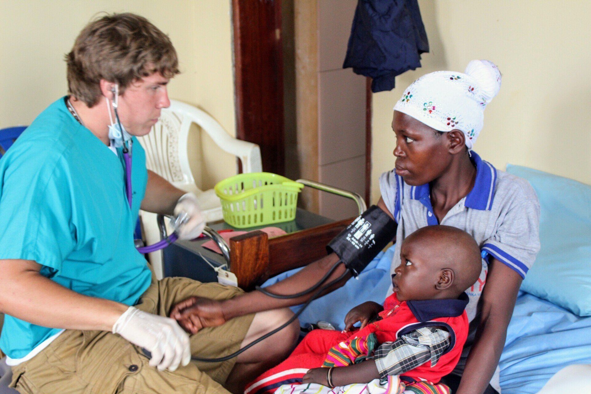 A doctor checks a child's blood pressure. The child sits with their mother in a clinic setting.