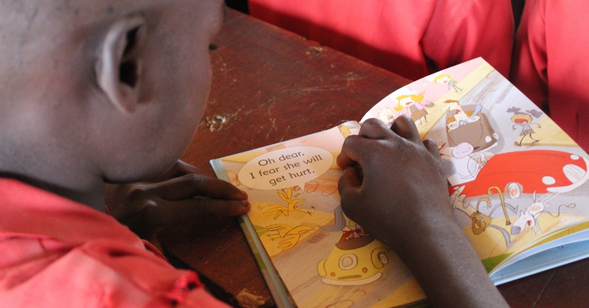 A boy is reading a book with a picture of a car on the cover