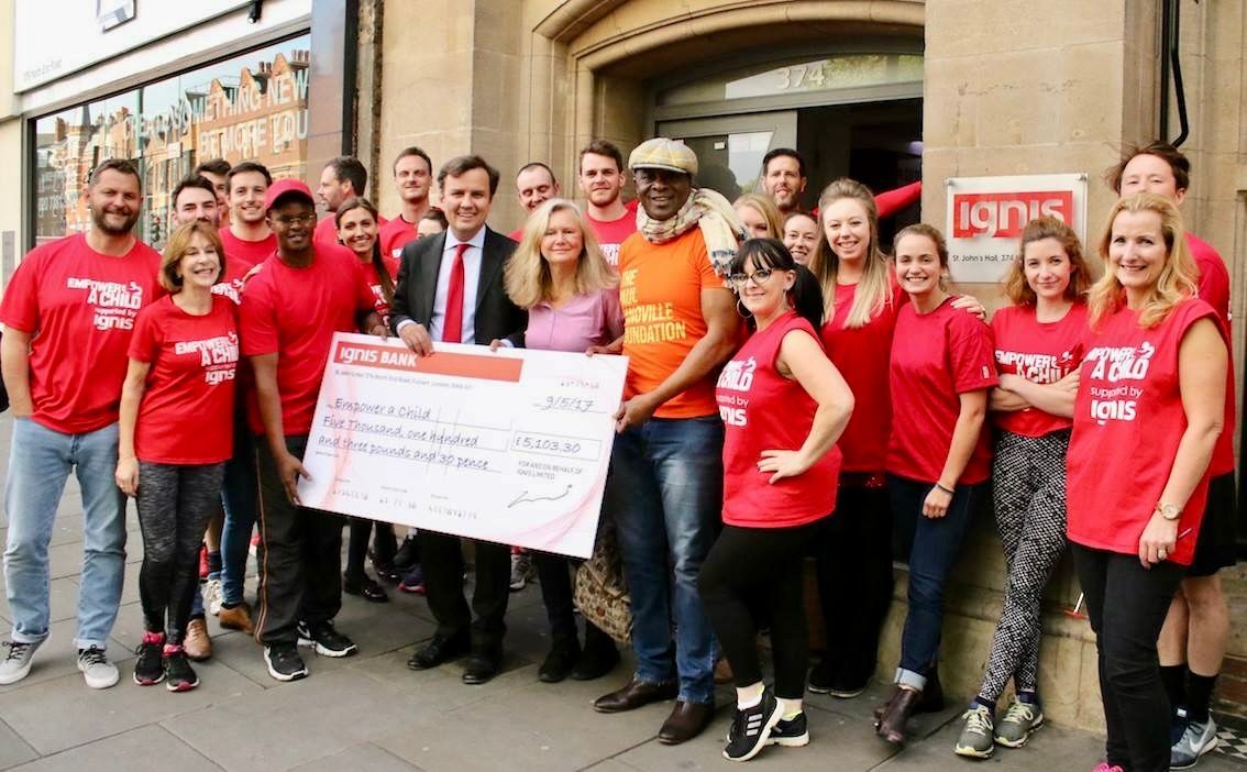 Group of people in red shirts holding large check in front of building.