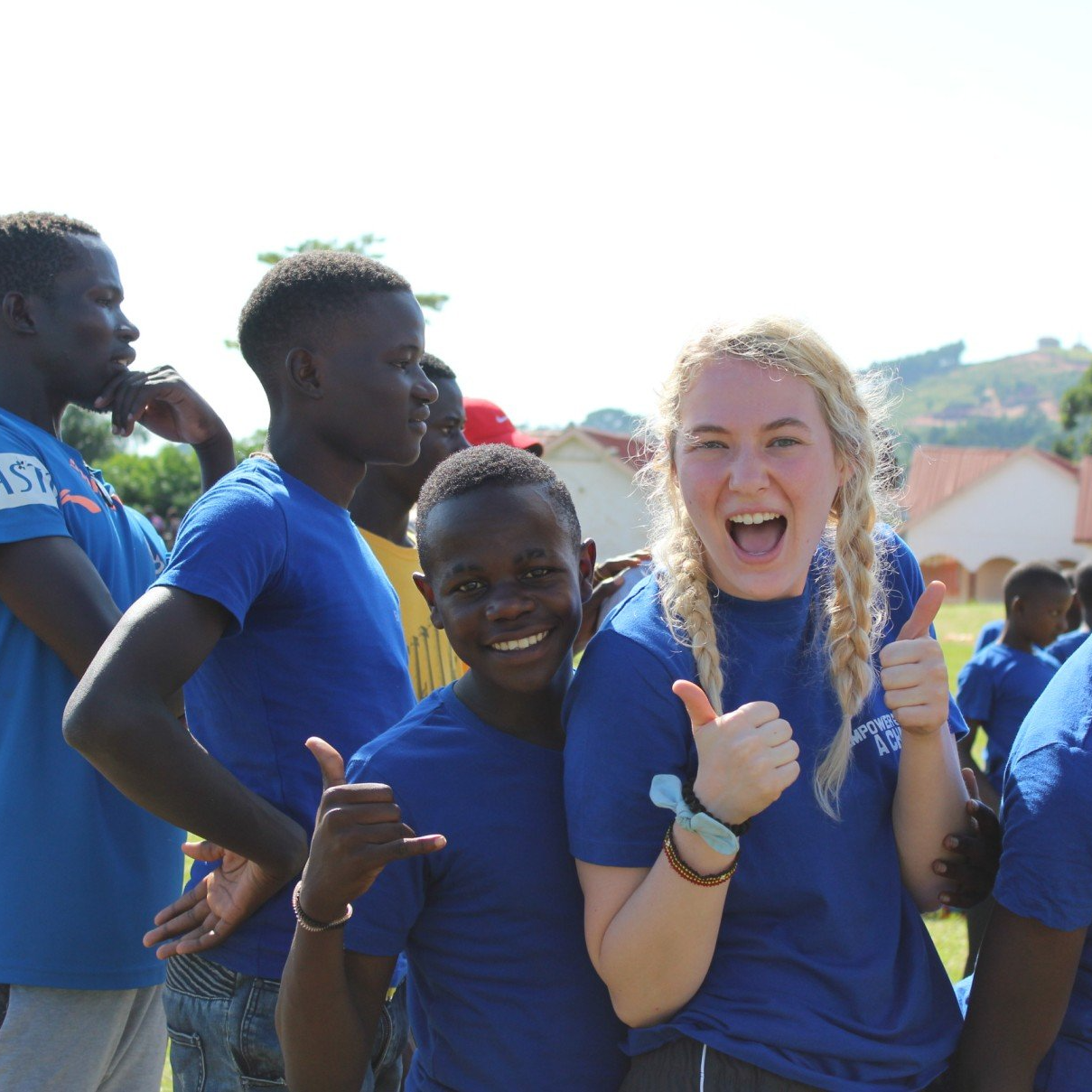 A diverse group of people in blue shirts smile. One young woman and boy give thumbs-up and hang loose signs.