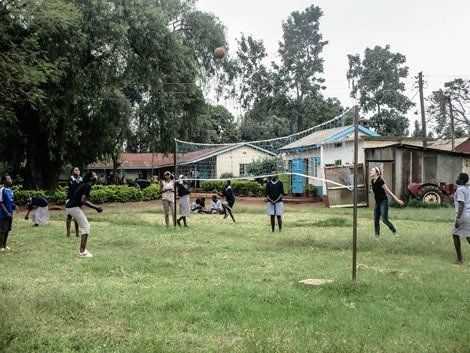 People playing volleyball on a grassy field near buildings.