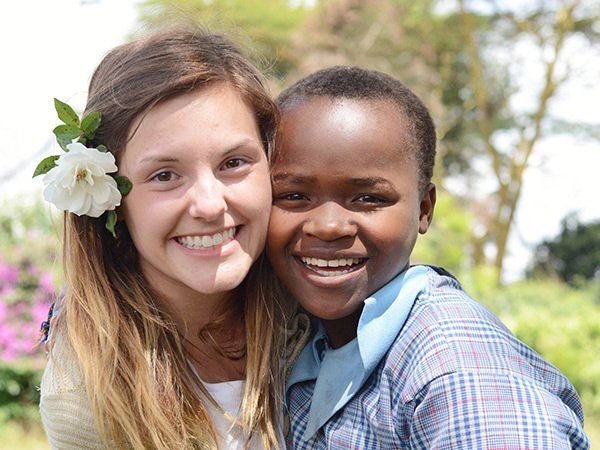 Woman with flower in her hair and African child smiling close together outdoors.