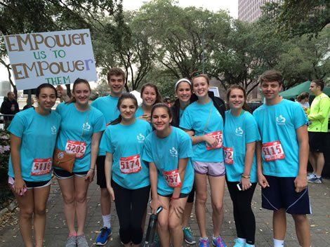 Group of teens in blue shirts at a race holding a sign, 