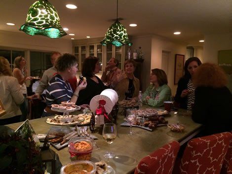People at a kitchen gathering, socializing around a counter laden with treats and drinks.