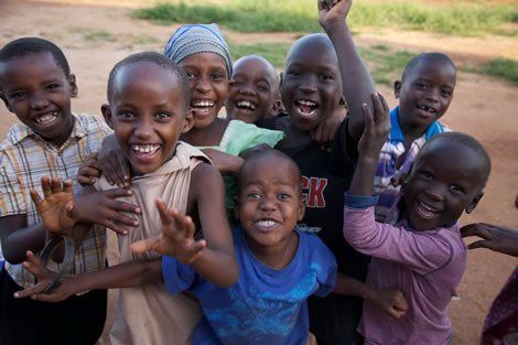 Group of smiling African children, embracing outdoors, some waving.