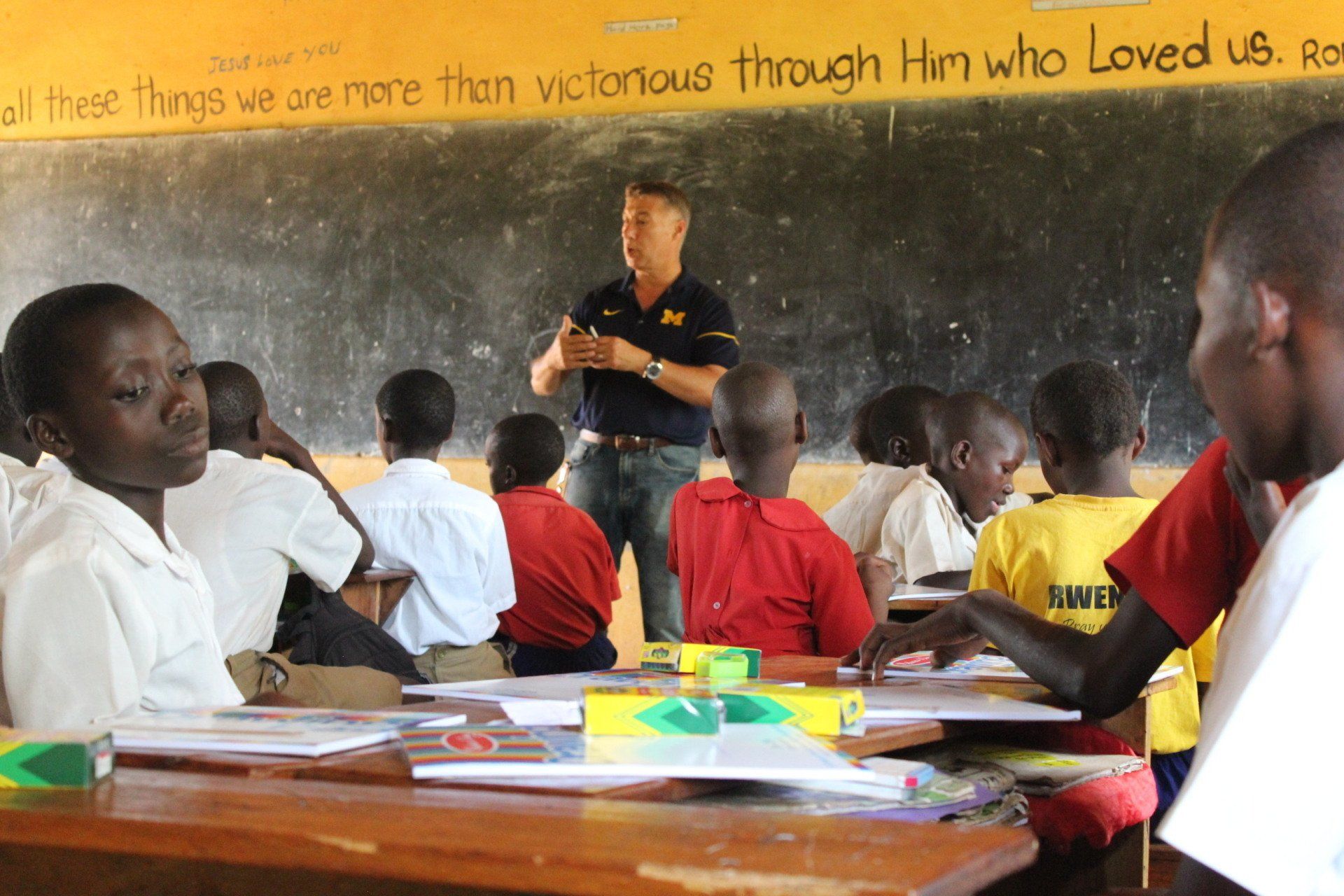 A man teaching a class of African students in a classroom. Students are seated at desks.