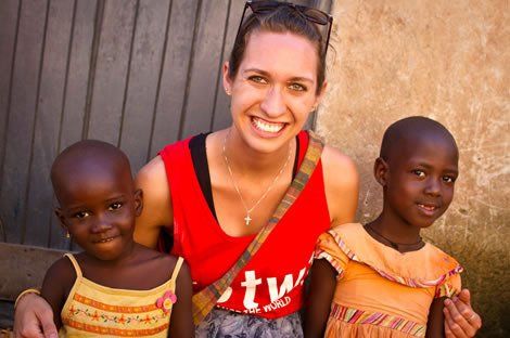 Woman in red top smiles with two African children; outdoor setting.