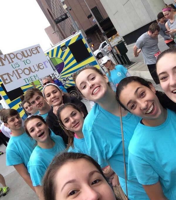 Group of smiling teens in blue shirts holding sign 