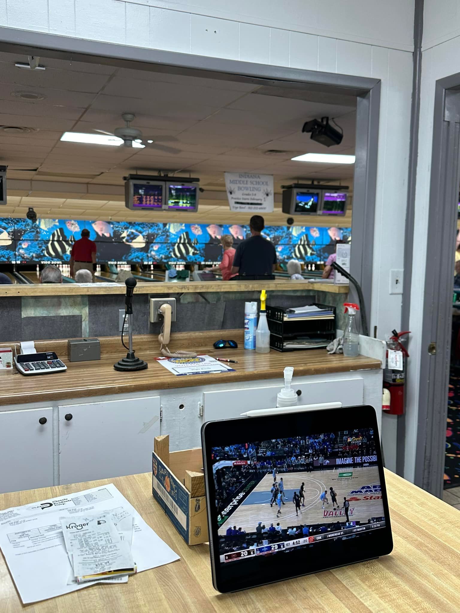 A tablet is sitting on a wooden table in front of a bowling alley.