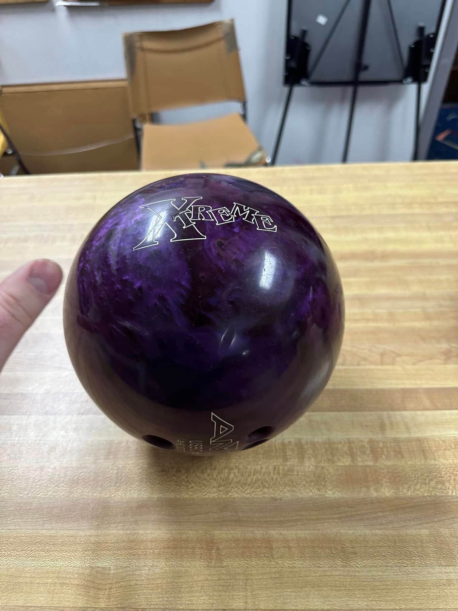 A person is holding a purple bowling ball on a wooden table.
