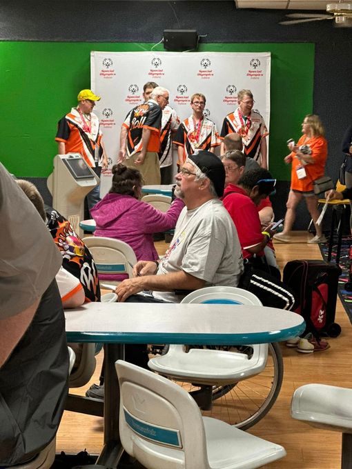 A group of people are sitting at tables in a bowling alley.