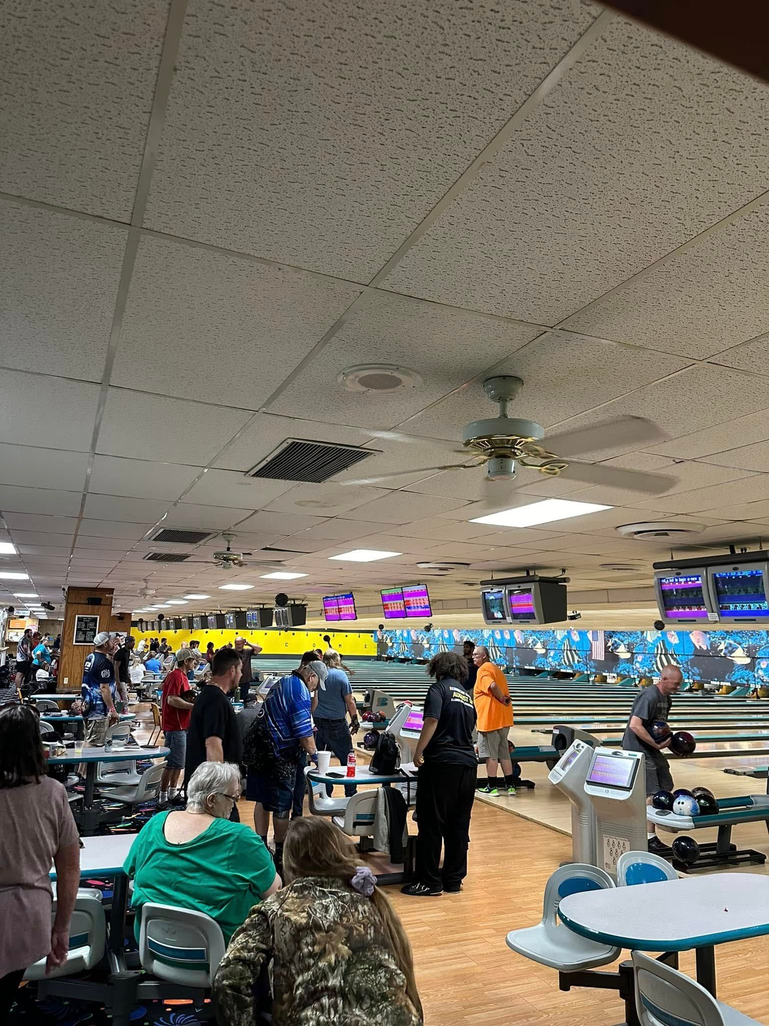 A group of people are sitting at tables in a bowling alley.