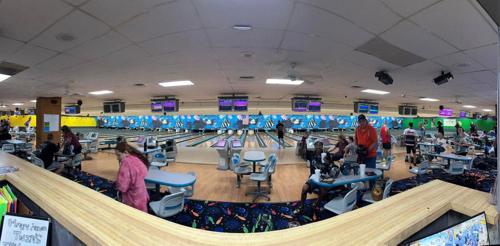 A panoramic view of a bowling alley with people playing bowling.