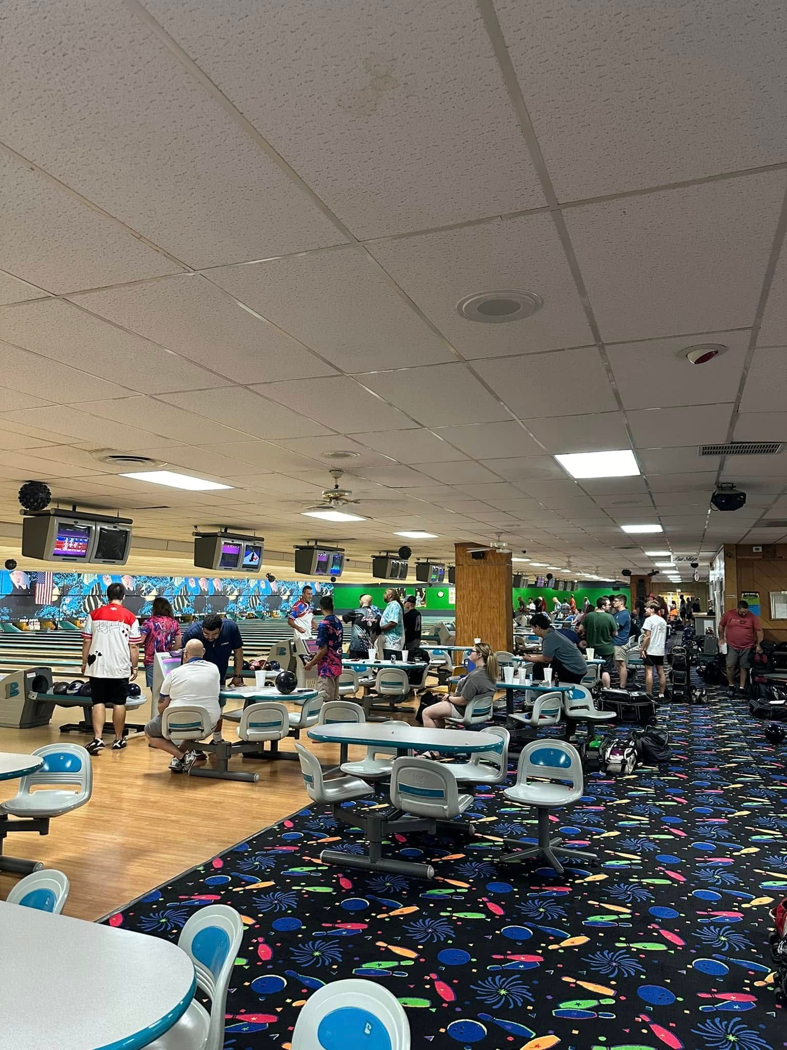 A bowling alley filled with people and tables and chairs.
