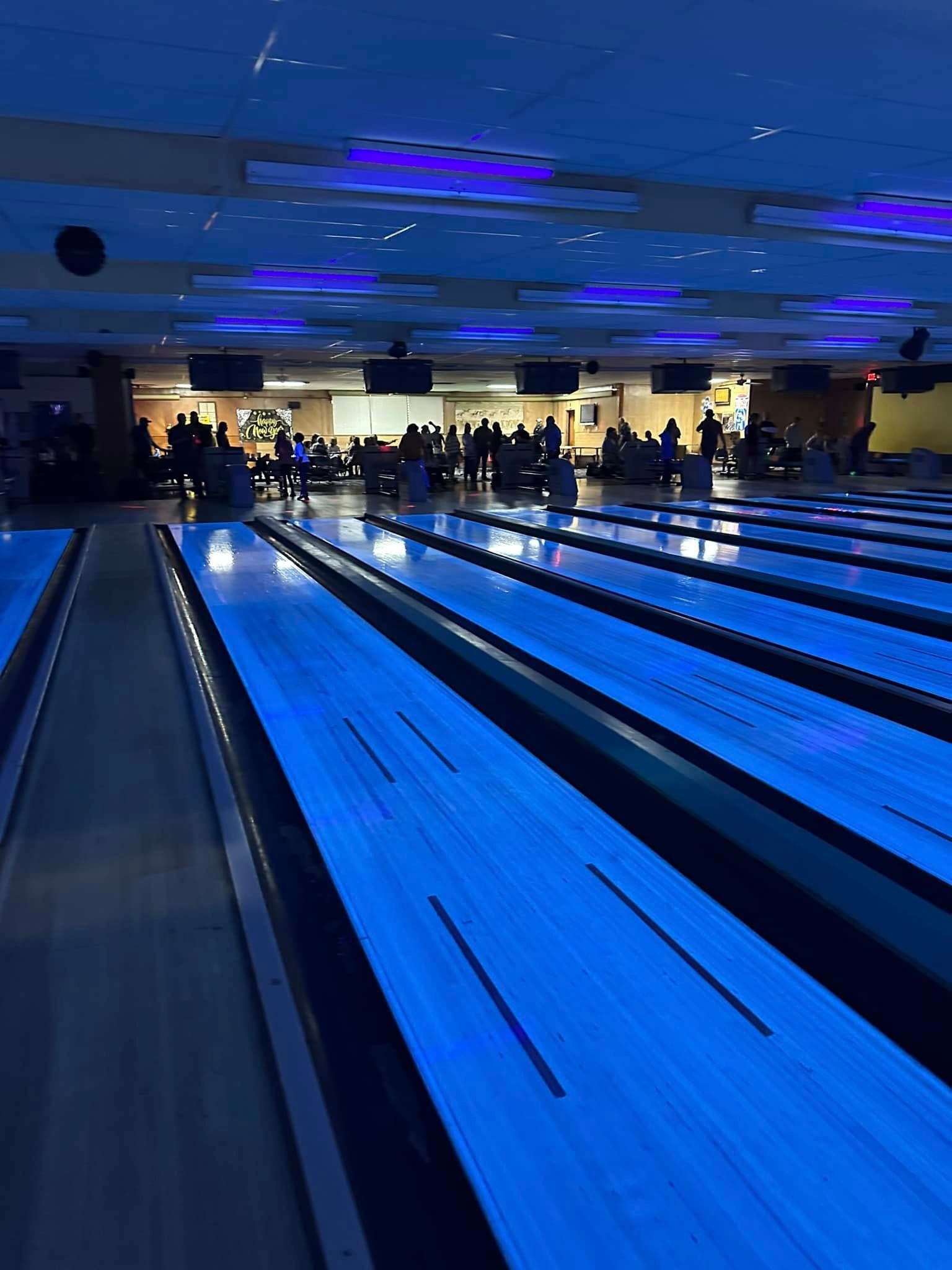 A group of people are playing bowling in a bowling alley at night.