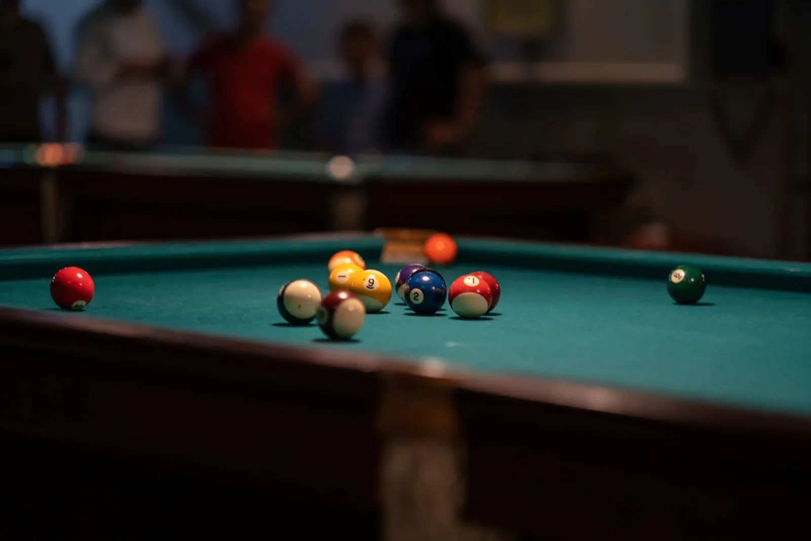 Pool table with balls scattered on green felt, people watching in the background.