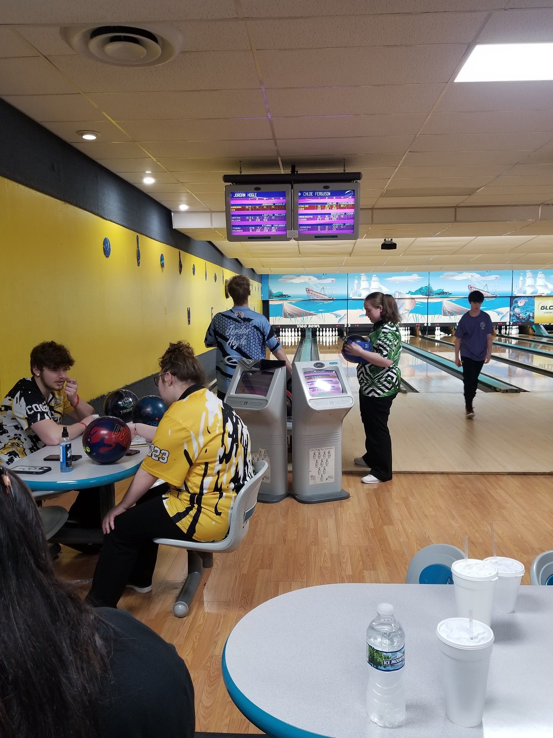A group of people are sitting at tables in a bowling alley.