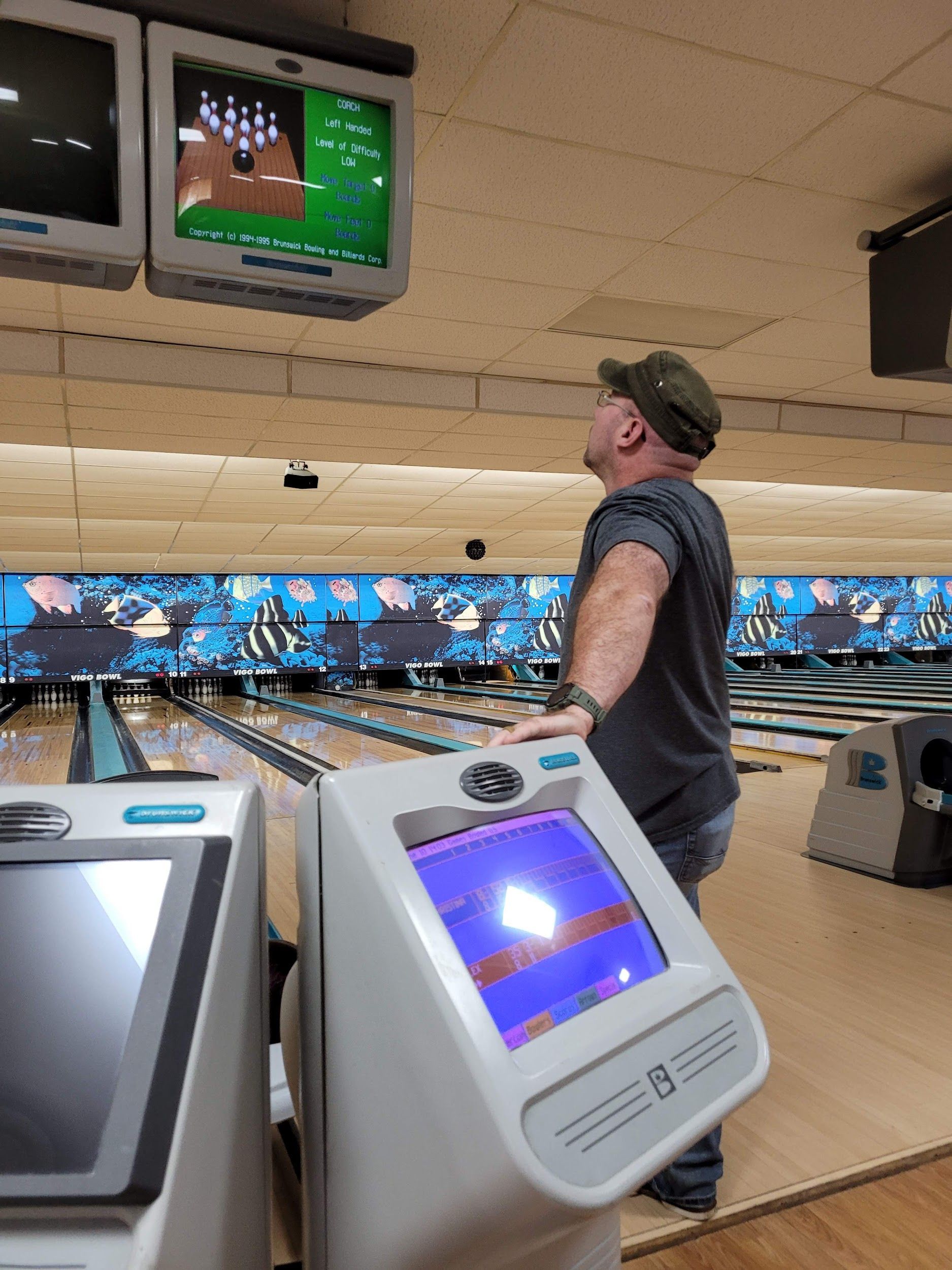A man is standing in a bowling alley looking at a monitor