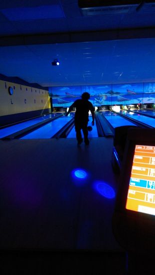A person is bowling in a dark bowling alley.