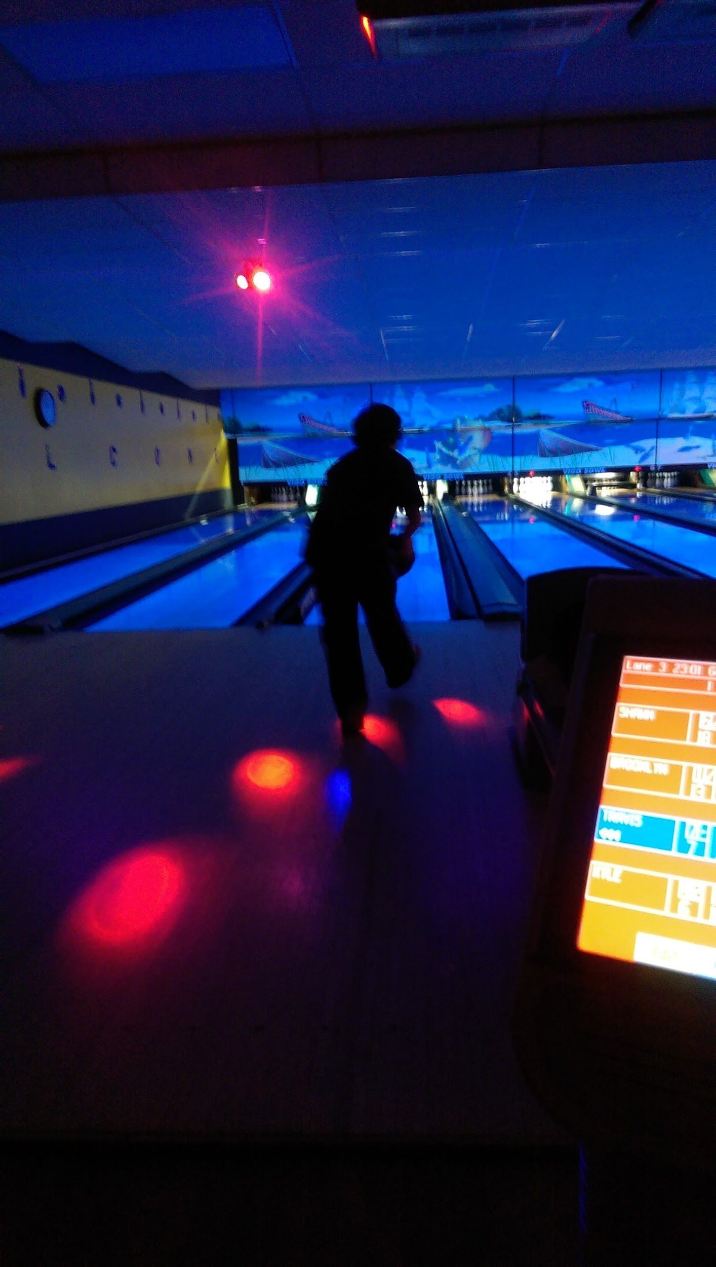 A person is playing bowling in a dark bowling alley