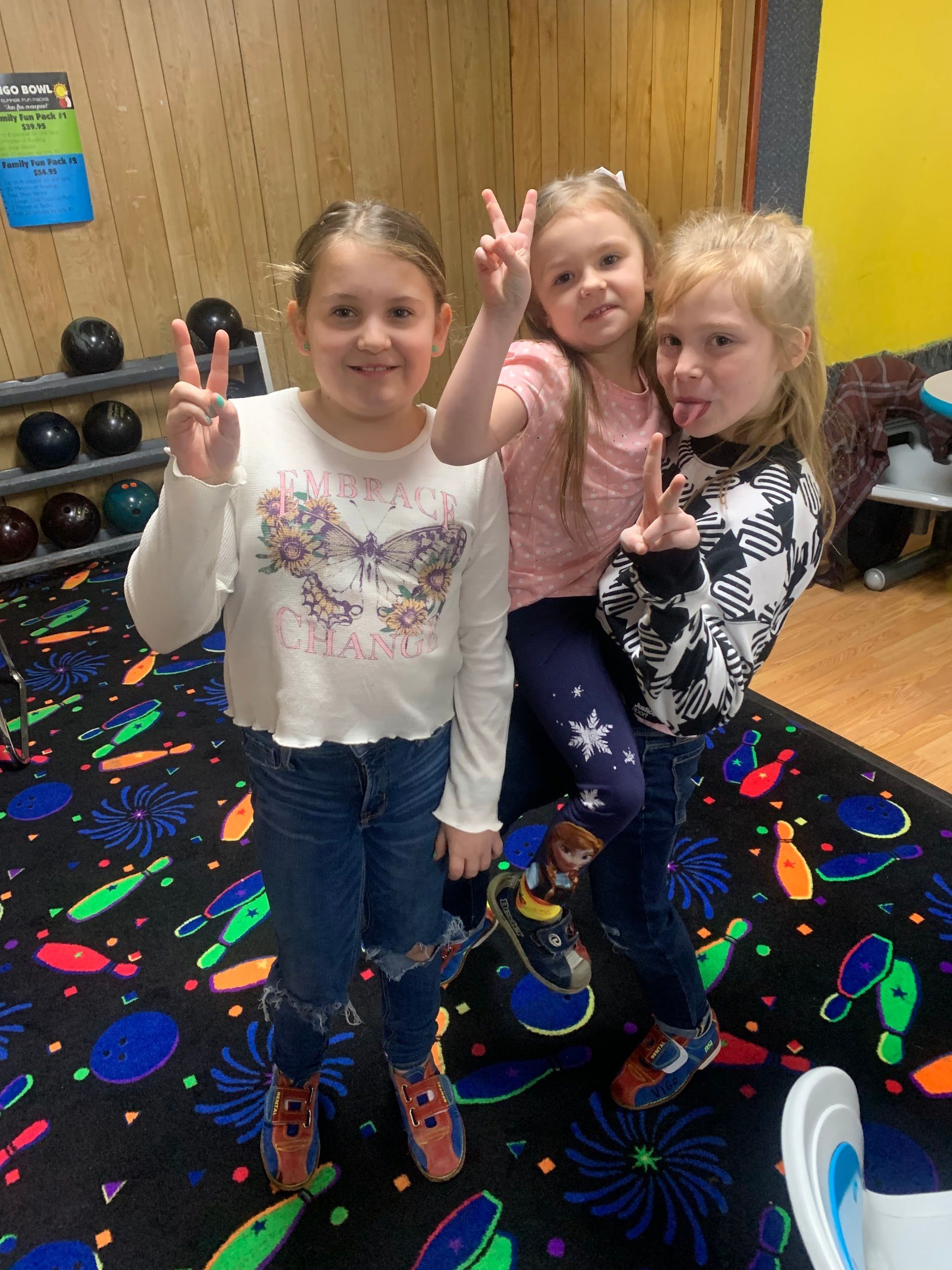 Three young girls are posing for a picture in a bowling alley.