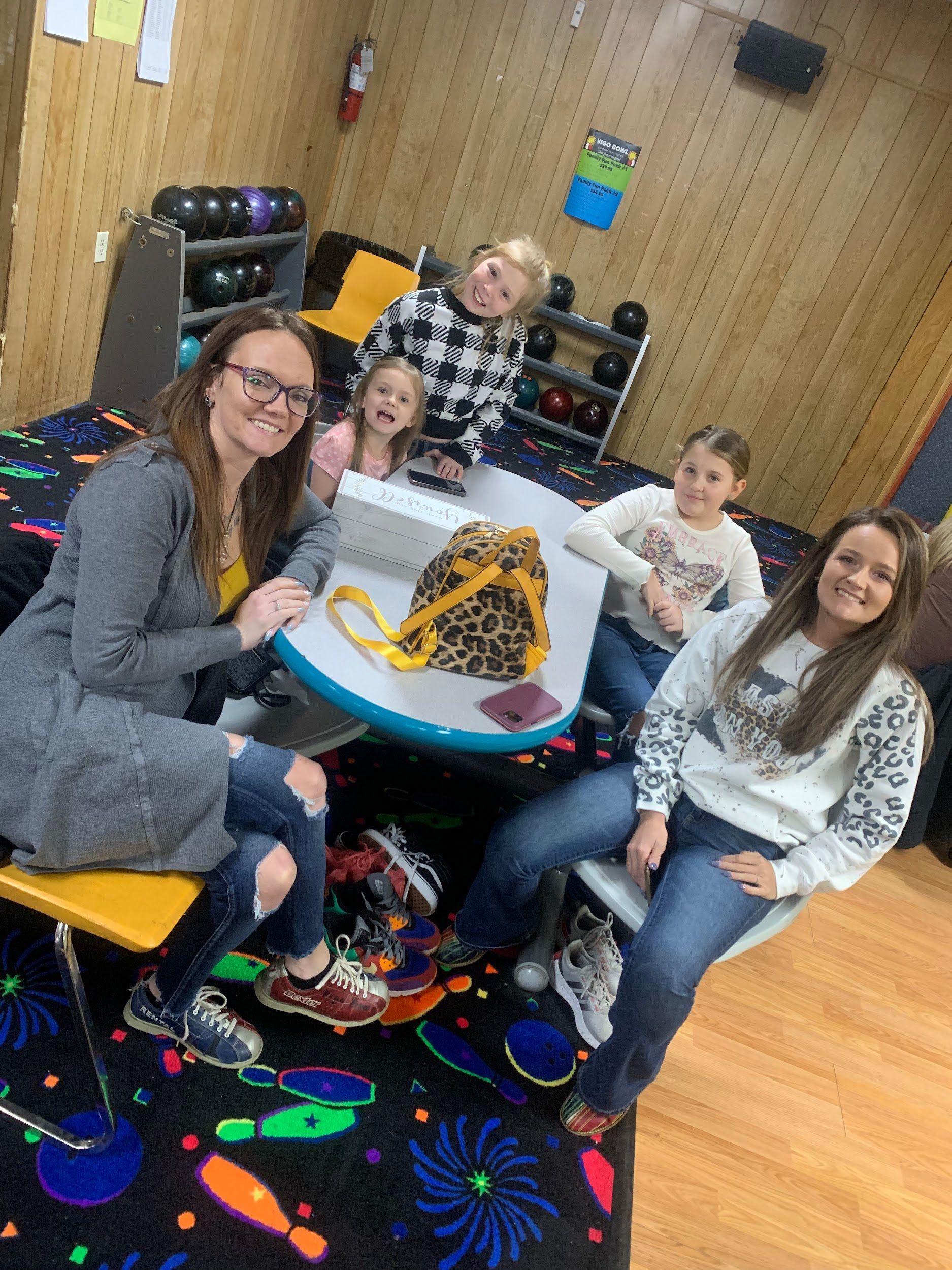 A group of people are sitting around a table in a bowling alley.