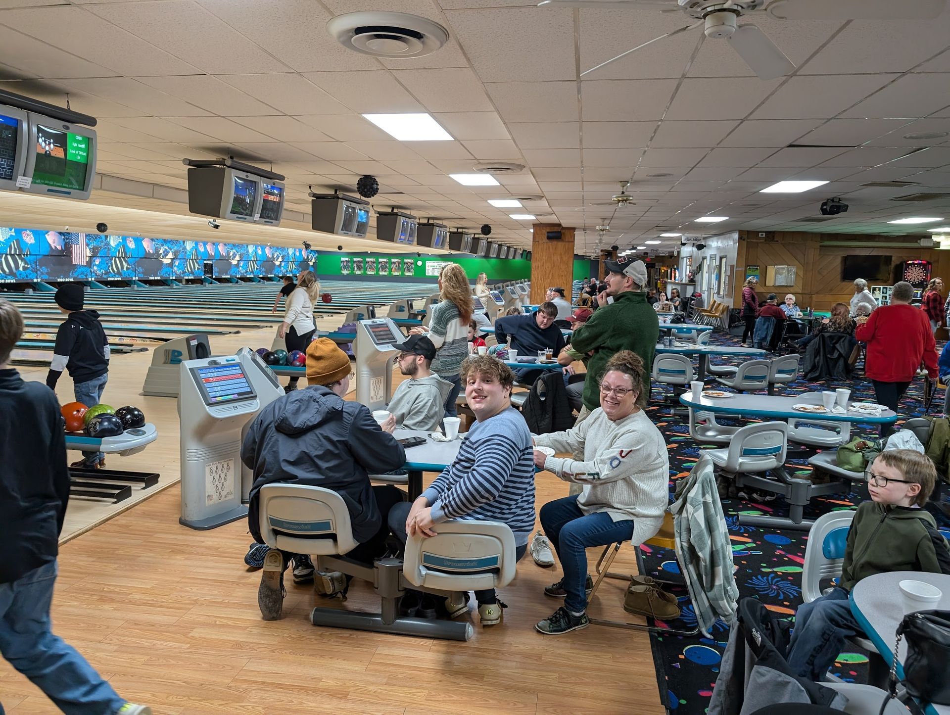 A group of people are sitting at tables in a bowling alley.