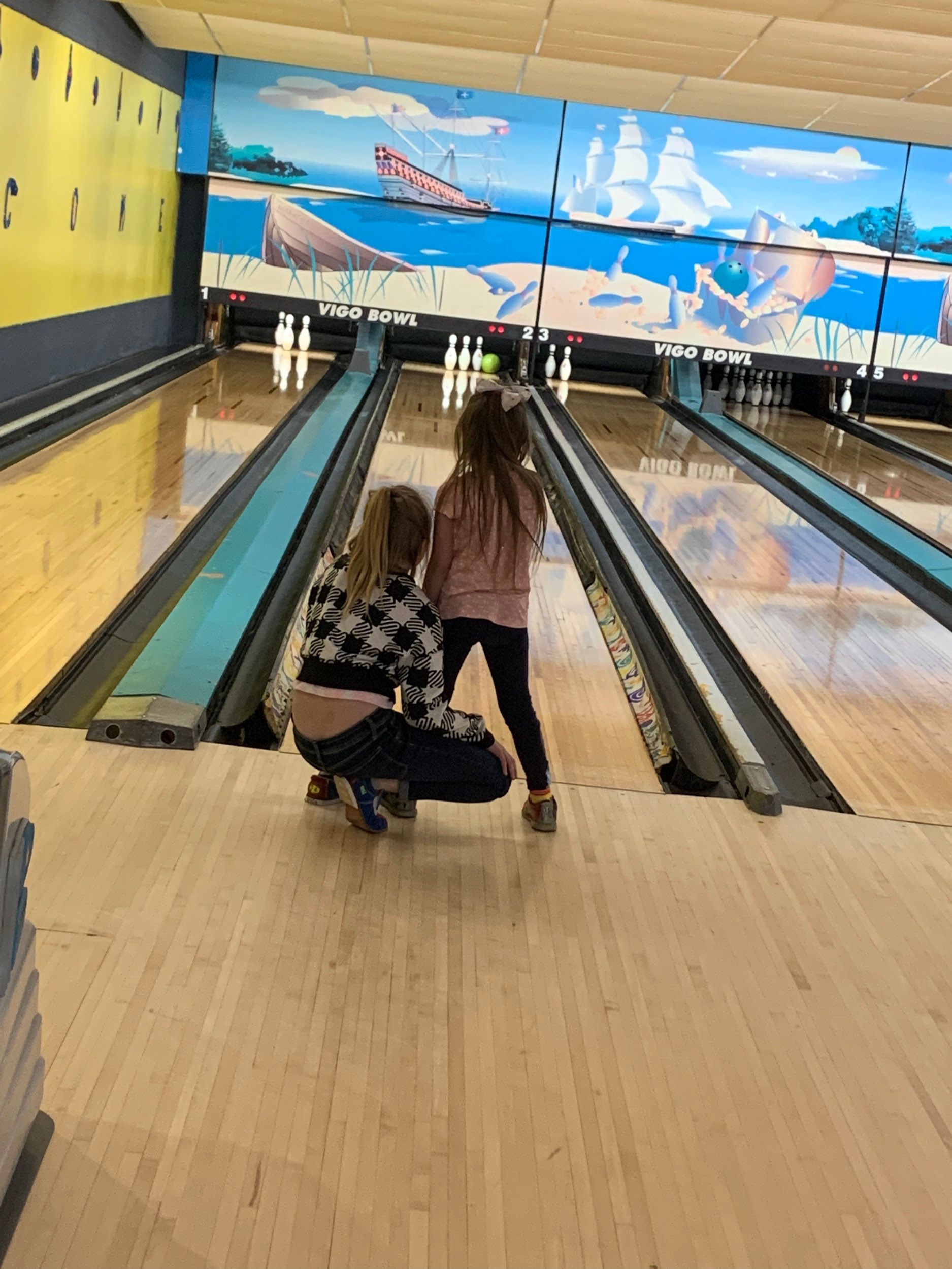 A woman and a little girl are playing bowling in a bowling alley.