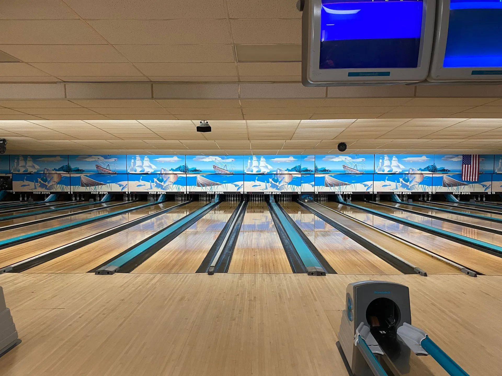 Bowling alley lanes viewed from behind the foul line. Blue and tan colors. Nautical-themed mural.