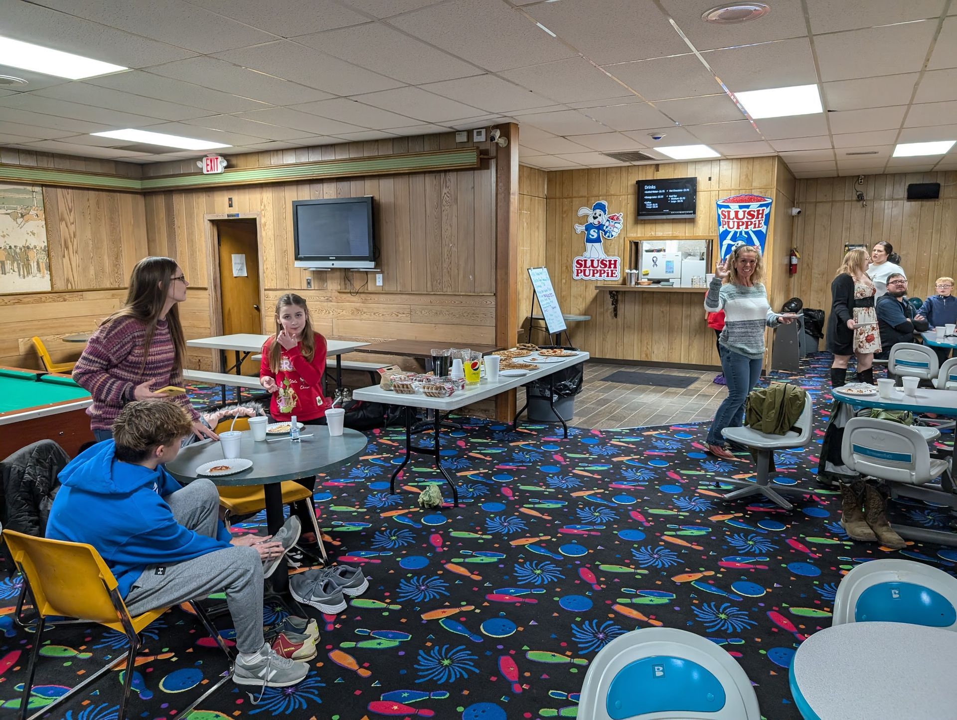 A group of people are sitting at tables in a bowling alley.