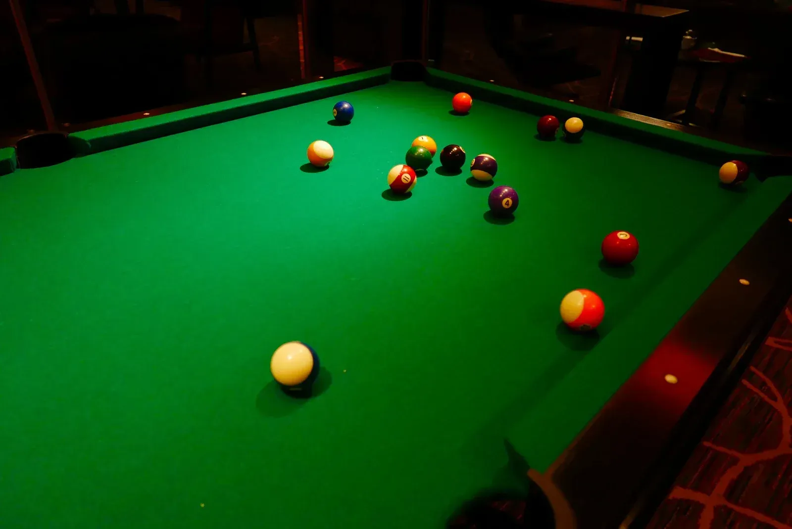 A pool table filled with pool balls in a dark room.