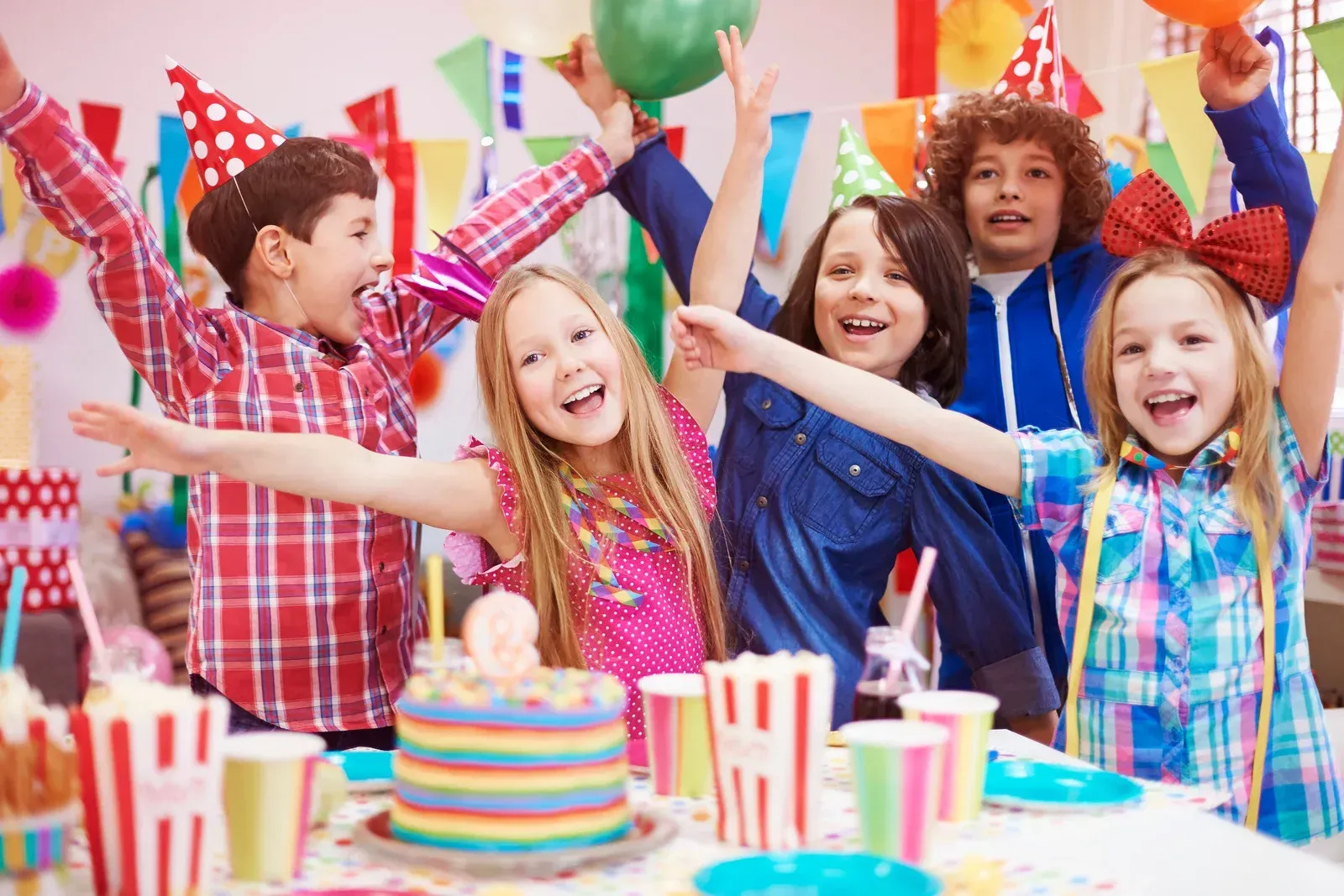 A group of children are sitting at a table with their arms in the air at a birthday party.