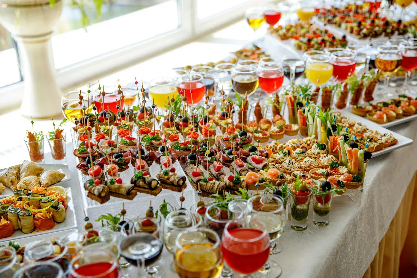 A buffet table filled with lots of food and wine glasses.
