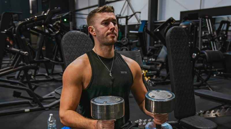 A man is holding two dumbbells in a gym.