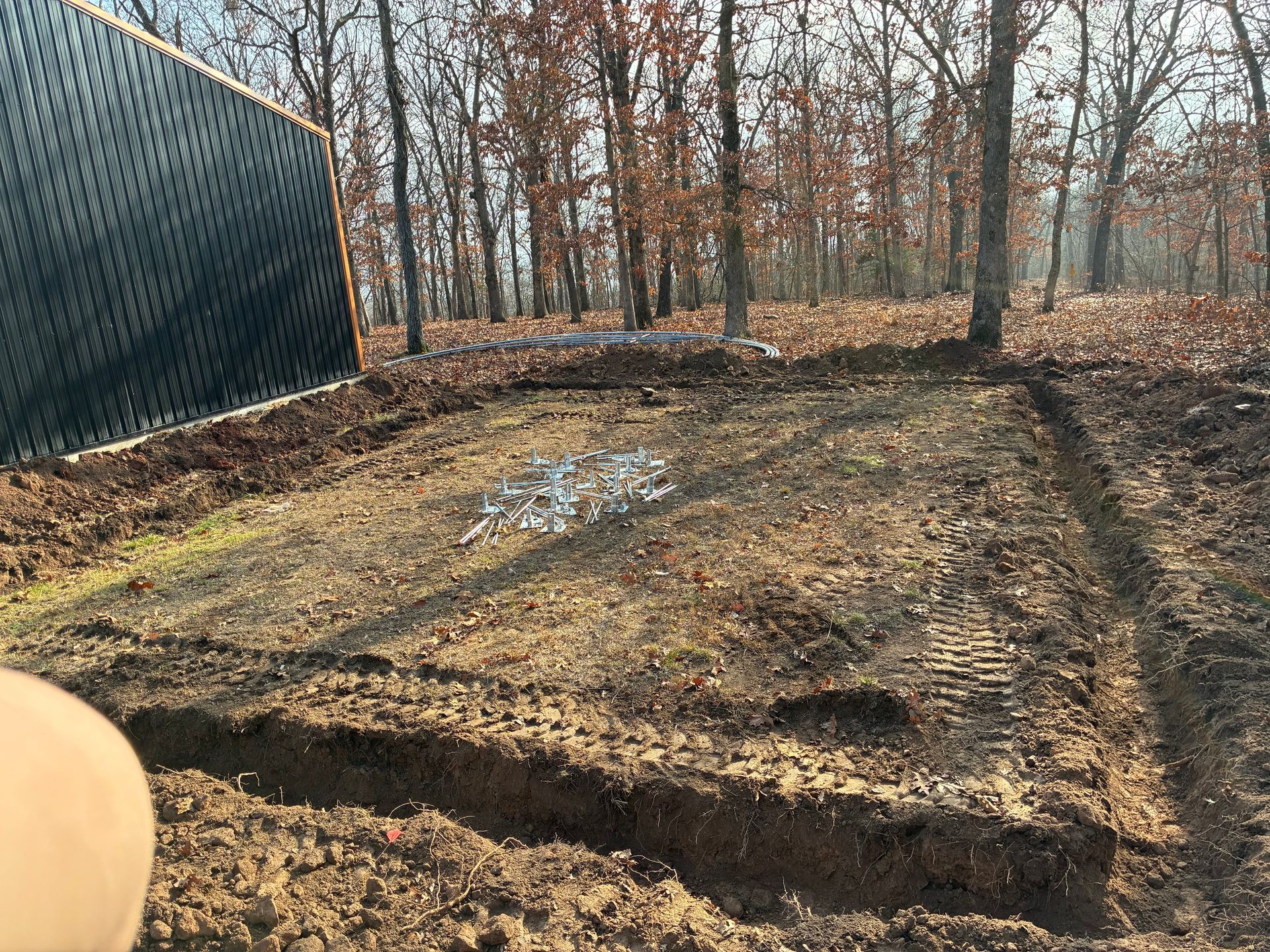 Cleared patch of dirt in woods, with a black panel at left and tire tracks visible.