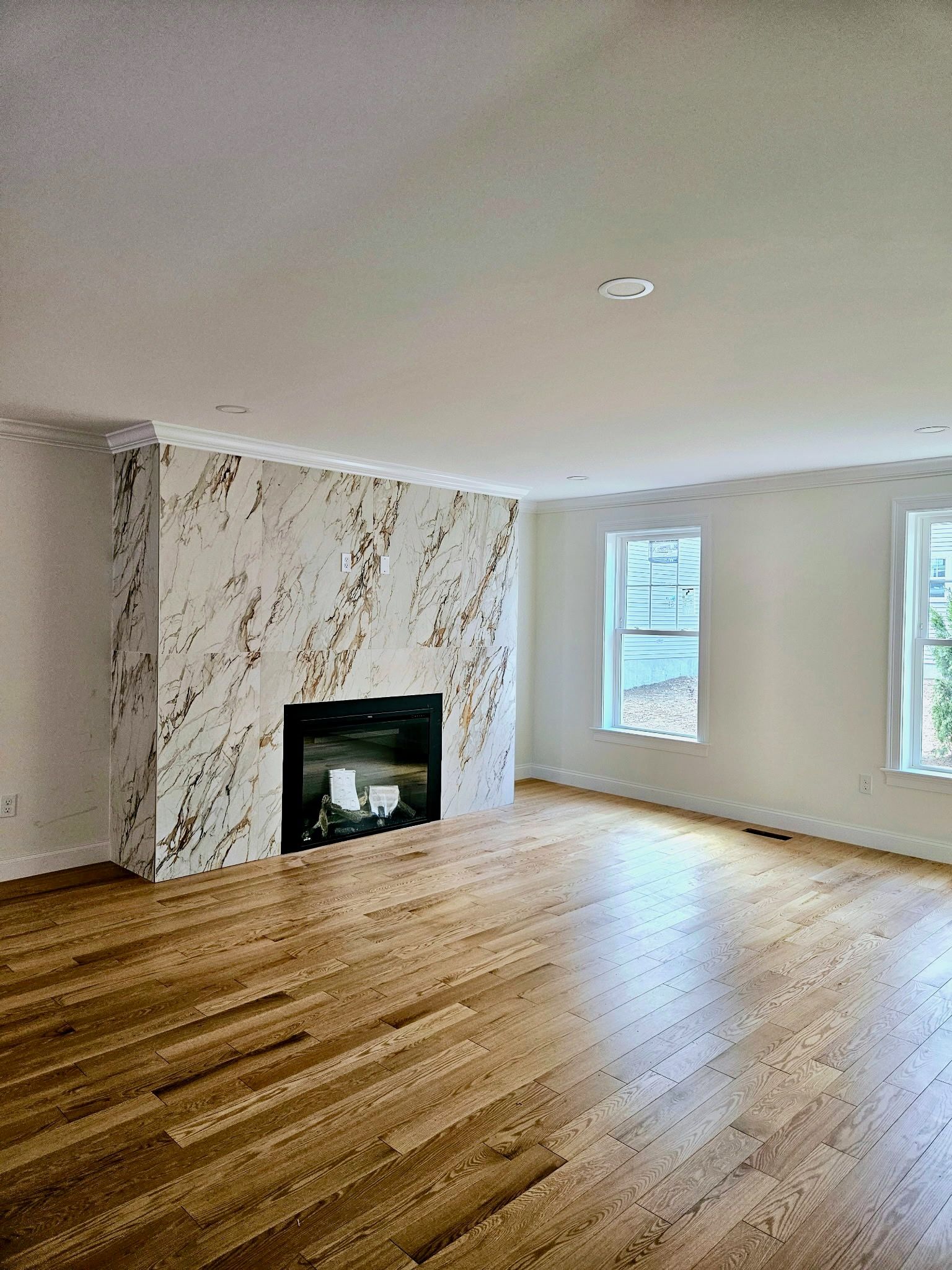 Living room with marble fireplace, hardwood floors, and two windows.
