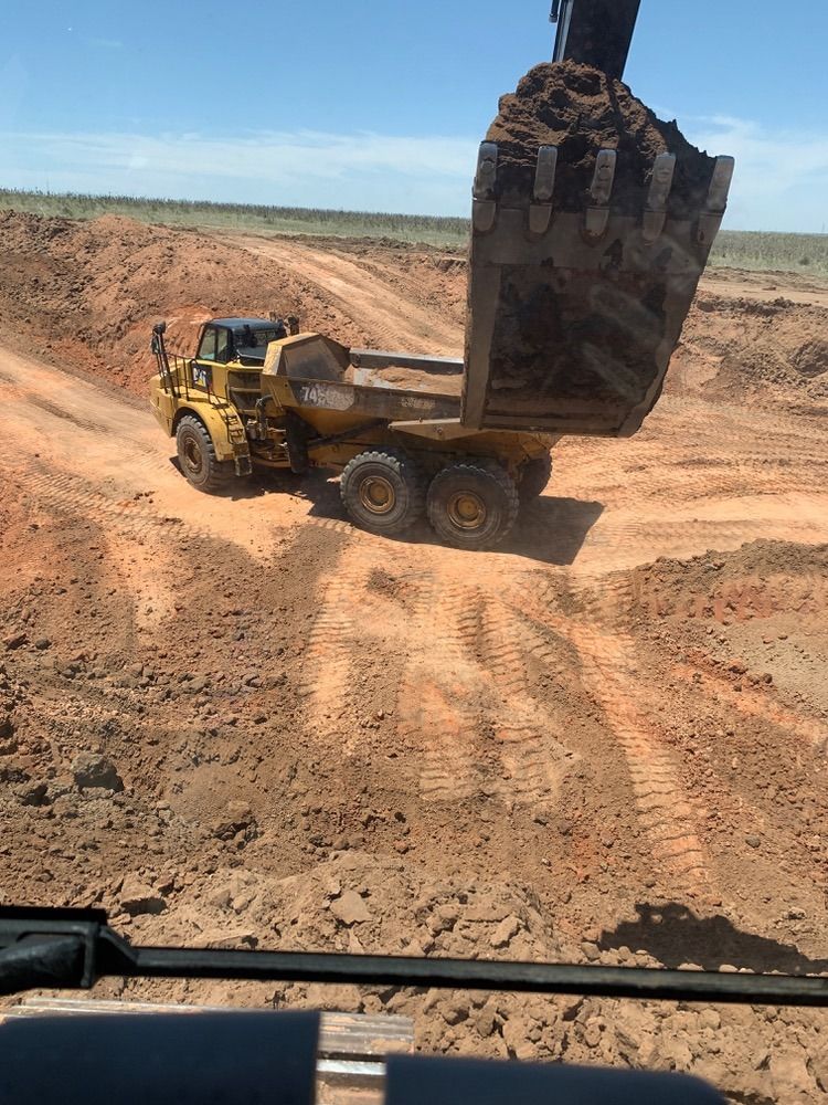 Yellow excavator loading brown soil into a yellow dump truck on a dirt lot.
