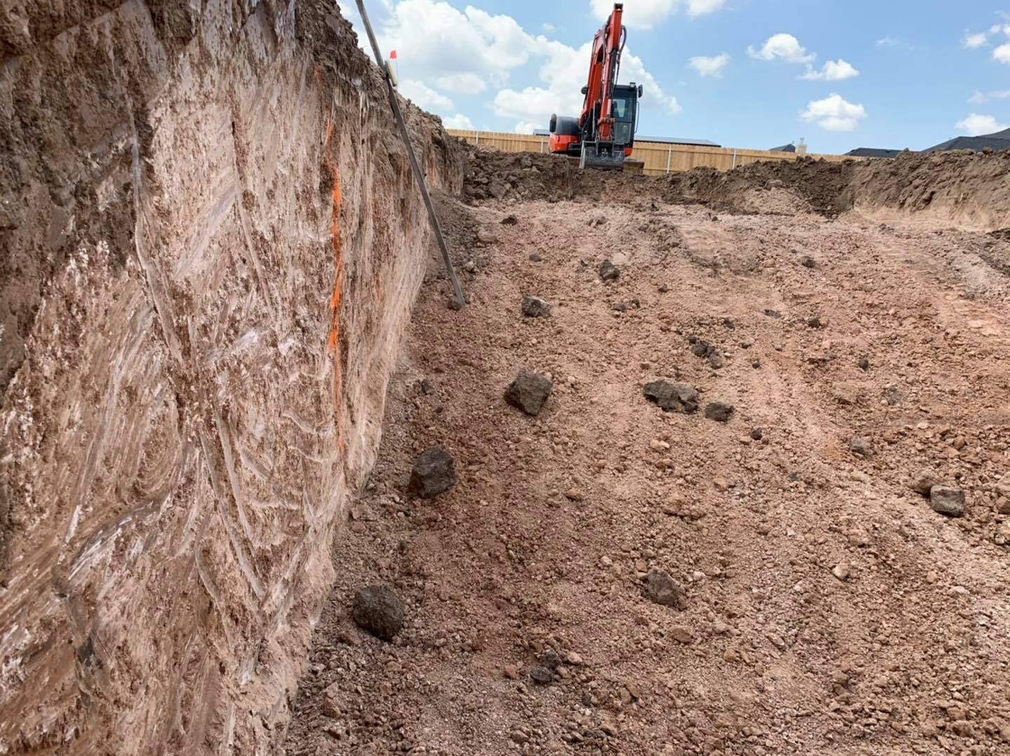 Excavation site with an excavator, red-brown dirt, and a vertical wall.