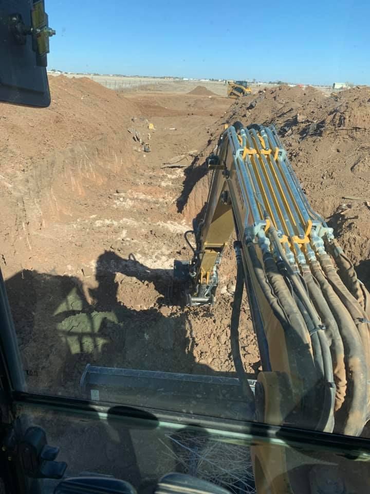 Excavator digging in a dirt pit on a construction site on a sunny day.