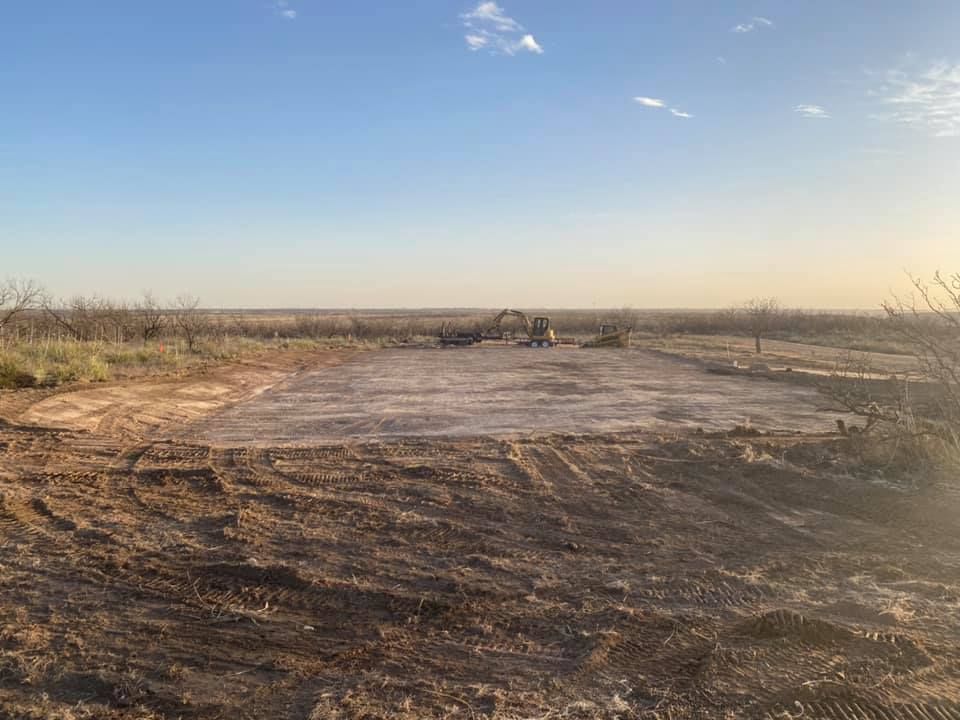 Dirt clearing for foundation in a field under a blue sky.