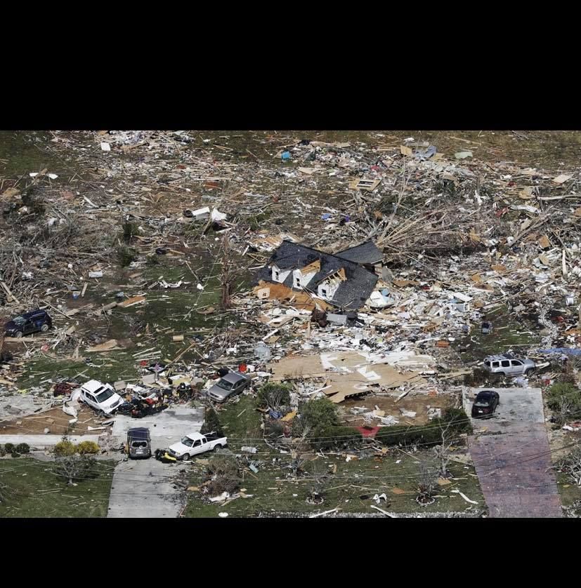 A house mostly intact surrounded by widespread destruction from a tornado.