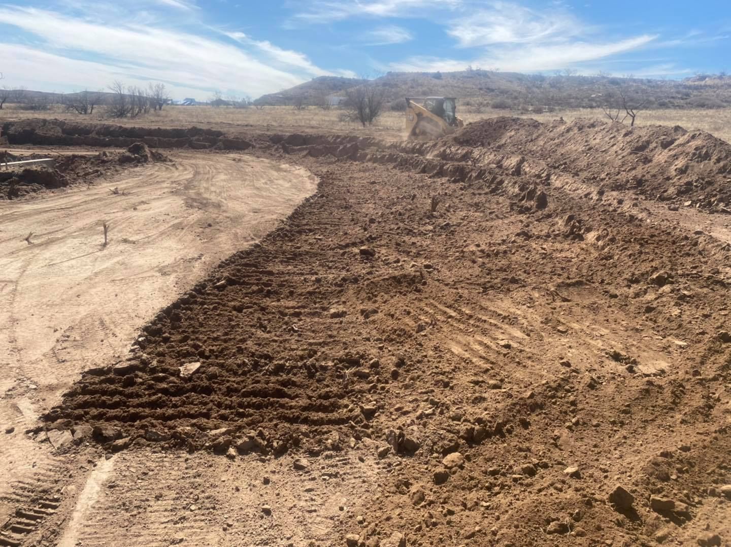 Dirt road construction with mounds of soil in a sunny, outdoor setting.
